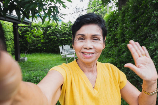 asiatische seniorin selfie während video-anruf mit familie - video voip fotos stock-fotos und bilder