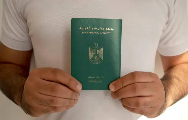 Egyptian passport in male hands. Man in white t-shirt is holding passport of Arab Republic of Egypt, light white background.