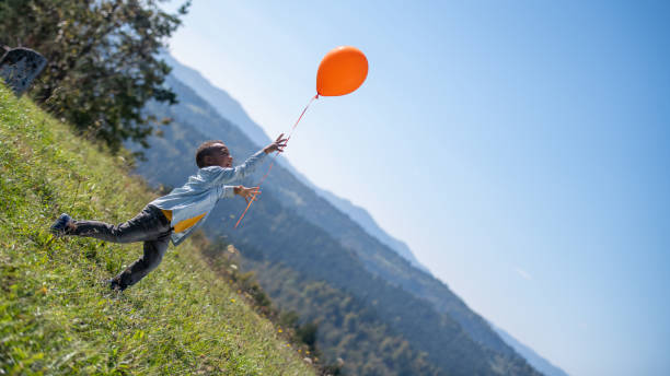 istock Boy on a meadow releasing an orange balloon 1251178584