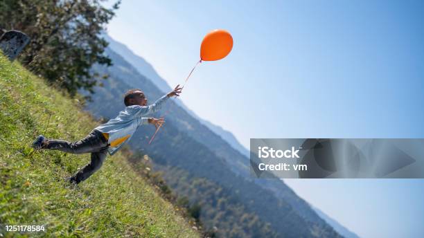 Boy On A Meadow Releasing An Orange Balloon Stock Photo - Download Image Now - Balloon, Child, Letting Go