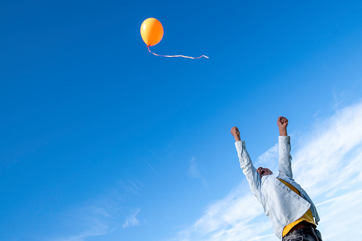 Little boy of African descent releasing an orange balloon into the sky.