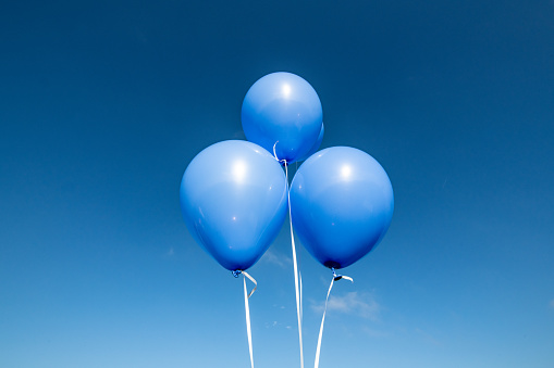 Three blue balloons photographed against a clear blue sky.