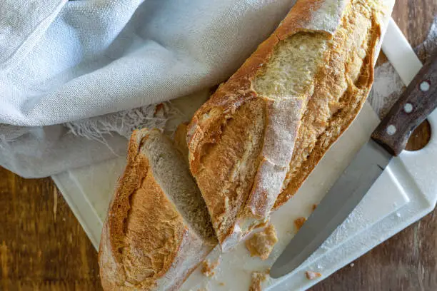 A fresh, crispy Italian bread, on a white cutting board on a wooden table and wheat flour.