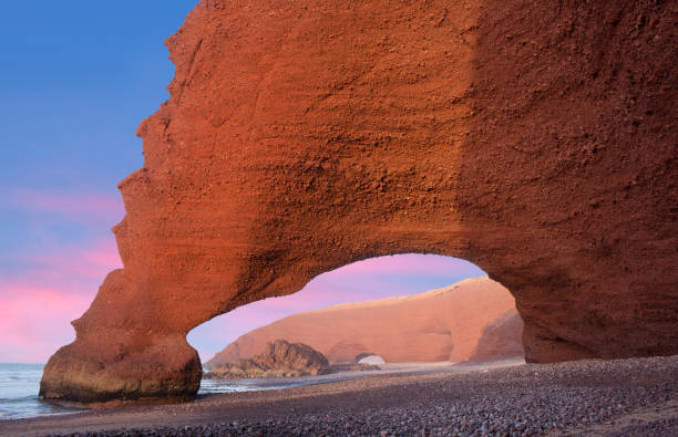 Red arches at Legzira beach near Sidi Ifni on Atlantic coast in Morocco, North Africa View of Red arches on Legzira beach near Sidi Ifni on Atlantic coast in Morocco, Northern Africa. One of two rock archways has collapsed in 2016. sunset agadir marocco stock pictures, royalty-free photos & images
