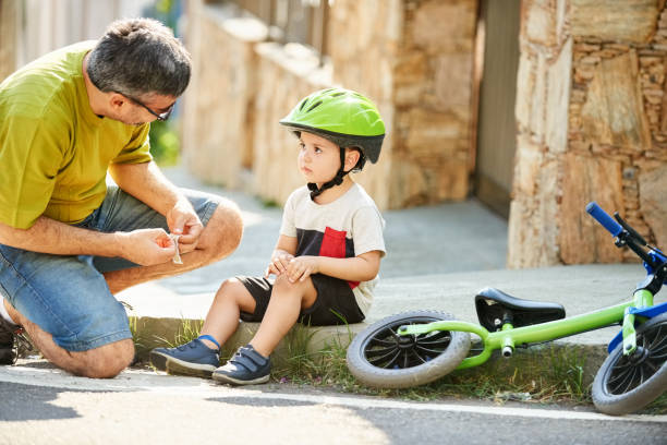 It's just a little scrape Shot of a little boy got fallen while riding his bicycle and father putting adhesive bandage over his knee injury man sitting with a bandage on his leg stock pictures, royalty-free photos & images
