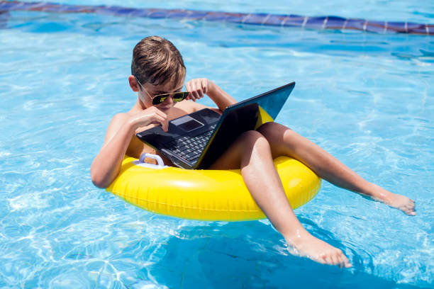 istock Kid boy using laptop in the swimming pool. Technology, summer and vacation concept 1251189984