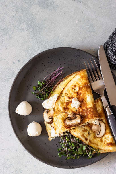 istock Classic egg omelette or omelet served with mushrooms, mozzarella and microgreens on black ceramic plate. Breakfast. Light grey stone background. 1251190606
