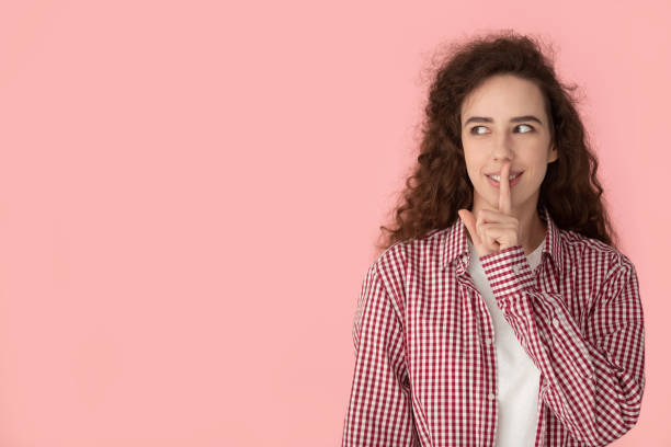 uśmiechnięta tysiącletnia dziewczyna patrzy na puste miejsce na kopiowanie na bok - finger on lips silence peeking women zdjęcia i obrazy z banku zdjęć