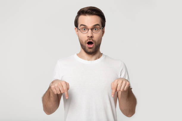 istock Surprised millennial guy in glasses point down demonstrating offer 1251198939