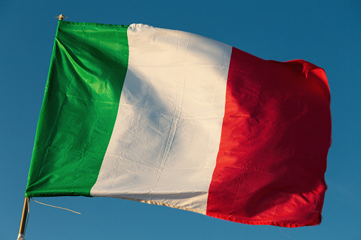 Italian flag flying in the wind with a blue sky background.