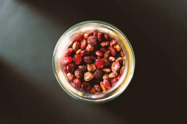 Sumac fruits in glass jar on black background. Spices from directly above, selective focus.