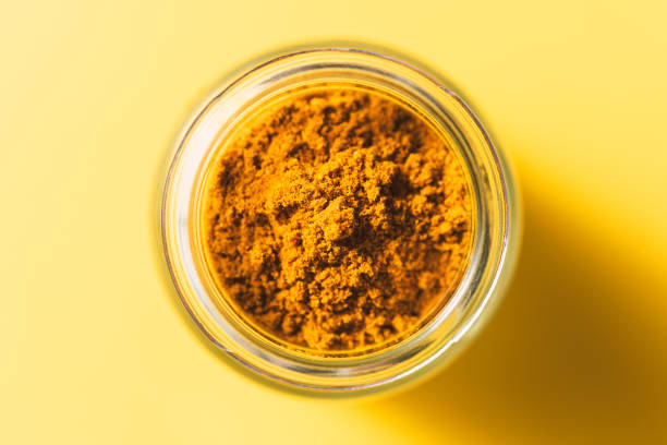 Curry powder in glass jar on yellow background. Spices from directly above, selective focus.