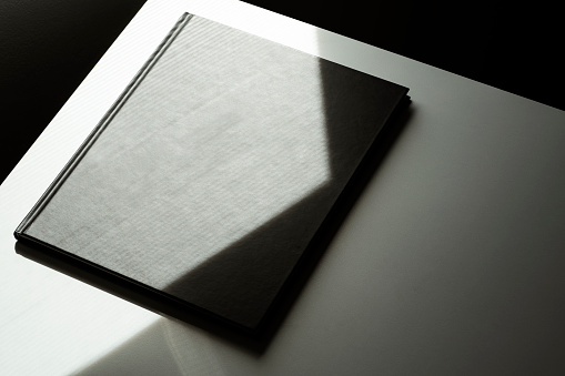 Black blank magazine cover mockup, template at the corner of the table with natural light and shadow