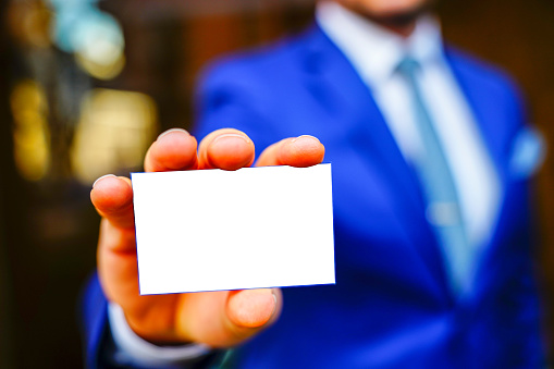 Young man in business suit holding white blank business card. Business name card presentation (mockup white card)