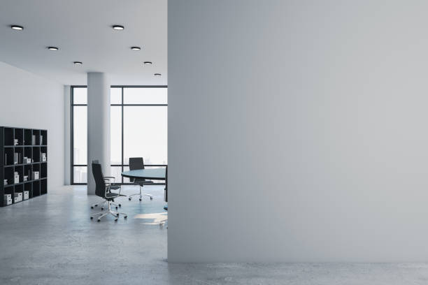 Empty office interior with a large empty white colored plaster wall and partly hardwood paneled wall with copy space on terrazzo floor. Wordesks, lighting equipment, computer equipment and windows in background. 3D rendered image.