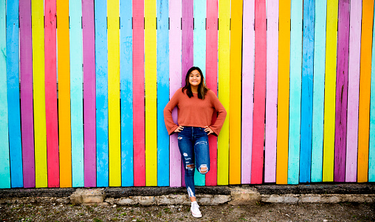 Fashionable high school girl stands against vibrant, multi-colored wall