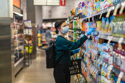 A woman browses the dry goods section at a local grocery store. She is wearing a protective face mask and gloves. Shopping during COVID-19 pandemic.