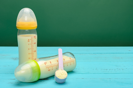 two glass baby bottles with powdered milk and a scoop nearby