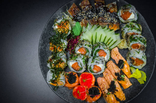 sushi, tradycyjne dania kuchni japońskiej. kilka pysznych sushi na zdobionym talerzu, czarne tło. grupa sushi, urakami, nigori, sushi jow, sashimi, tekamaki itp ... - niguiri sushi zdjęcia i obrazy z banku zdjęć