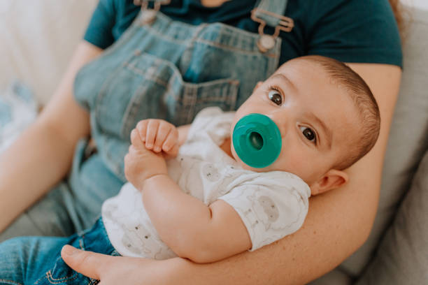 Mixed race mom holding her baby using pacifier stock photo
