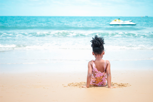 Cute kid setting and having fun on sandy summer beach with blue sea, happy little girl playing on tropical beach