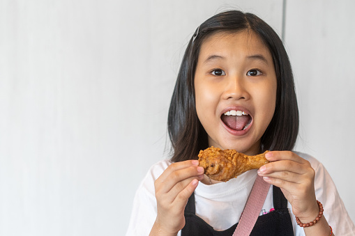 Portrait of an Asian Chinese little girl eating a fried chicken. She is looking at the camera with a big smile.