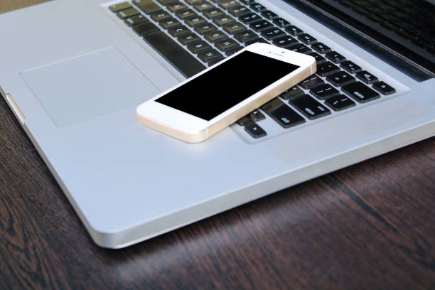 istock Mobile phone on laptop with wooden table 1251232967