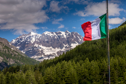 Italian flag winding in Gran Paradiso alpine landscape at springtime – northern Italy