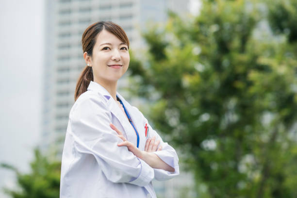 Asian female healthcare worker in white coat Asian female healthcare worker in white coat posing outdoors japanese female doctor stock pictures, royalty-free photos & images