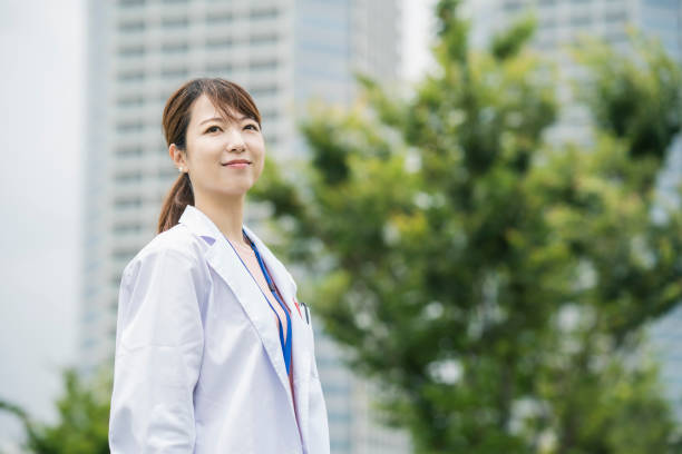 Asian female healthcare worker in white coat Asian female healthcare worker in white coat posing outdoors japanese female doctor stock pictures, royalty-free photos & images
