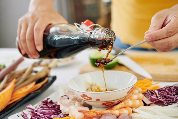 Woman pouring soy sauce into small bowl Woman pouring couple of tea spoons of soy sauce into small bowl when making dipping sauce for snack plate soy sauce photos stock pictures, royalty-free photos & images