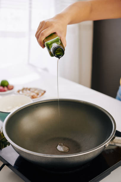 cocine vertiendo aceite vegetal - cazuela fotografías e imágenes de stock