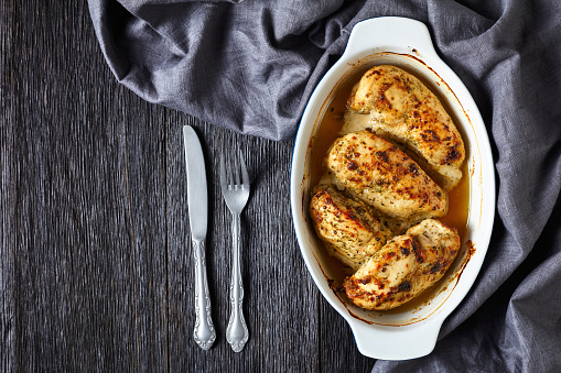 oven baked spicy juicy chicken breasts in a baking dish on a dark wooden table, flat lay, free space, horizontal view from above
