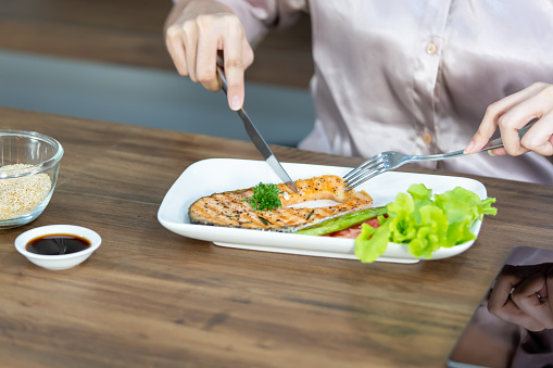 Women looking and eating salmon steak on white plate on table.