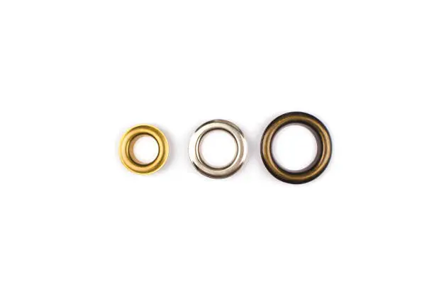 Three brass multicoloured metal eyelets or rivets - curtains rings for fastening fabric to the cornice, isolated on white. With copyspace for text for your presentation