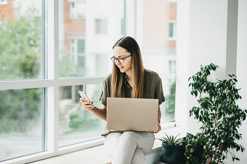 Young beautiful girl or student uses a laptop and cell phone or mobile phone.