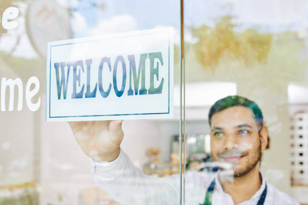 Smiling bakery shop owner sticking welcome sign on glass wall