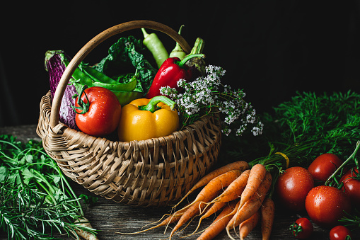 Fresh vegetables in a wicker basket and on a wooden table. Fresh groceries on kitchen table.