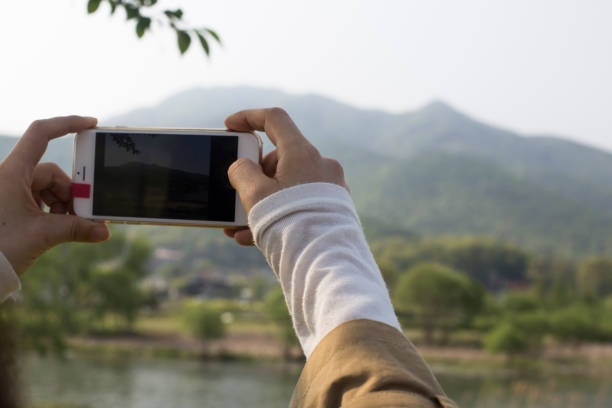 istock Using smart phone, woman photographs spring landscape with green tree. 1251271132