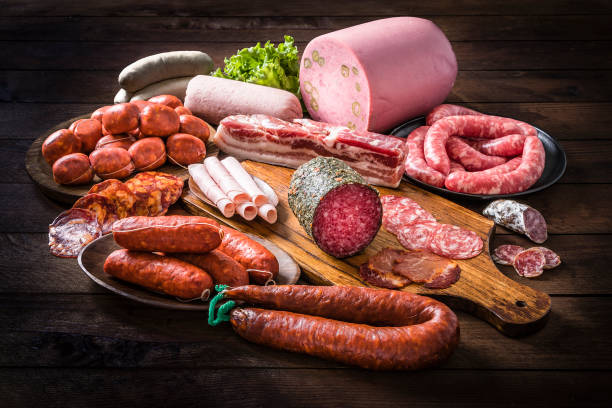 Front view of various kinds of raw sausages like mortadella, bacon, salami, ham and pickled sausages on a delicatessen concept background. Sausages are isolated at the center of the image on a rustic wooden table. Studio shot taken with Canon EOS 6D Mark II and Canon EF 24-105 mm f/4L