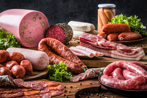 Front view of various kinds of raw sausages like mortadella, bacon, salami, ham and pickled sausages on a delicatessen concept background. Sausages are on a rustic wooden table. Studio shot taken with Canon EOS 6D Mark II and Canon EF 24-105 mm f/4L