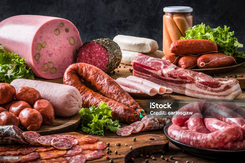 Various kinds of raw sausages on a rustic wooden table Front view of various kinds of raw sausages like mortadella, bacon, salami, ham and pickled sausages on a delicatessen concept background. Sausages are on a rustic wooden table. Studio shot taken with Canon EOS 6D Mark II and Canon EF 24-105 mm f/4L Meat Stock Photo