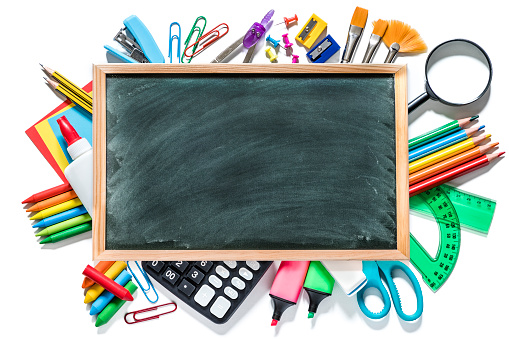 Top view of a blackboard surrounded and framed by various kinds of multicolored school supplies like scissors, crayons, rulers, pencils, papers, markers, calculators, magnifying glass, clips, thumbtacks, sharpeners and brushes isolated on white background. There is a useful copy space at the center of the image on the blackboard. Studio shot taken with Canon EOS 6D Mark II and Canon EF 24-105 mm f/4L