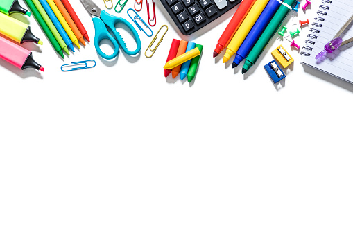 Top view of various kinds of multicolored school supplies like scissors, crayons, rulers, pencils, papers, markers, calculators, magnifying glass, clips, thumbtacks, sharpeners and brushes standing at the top of the image on a frame shape with copy space at the lower part of the image on a white background. Studio shot taken with Canon EOS 6D Mark II and Canon EF 24-105 mm f/4L