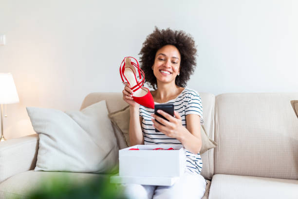 istock Smiling woman unboxing a postal parcel and taking a selfie with her new purchases using a smartphone. Showing shoes to her friends via video call 1251273032
