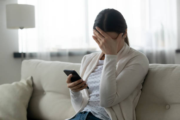 Stressed woman holding smartphone feels humiliated, cyberbullying concept Woman sit on sofa holding smartphone cover face with hand feels scared humiliated suffering from cyberbullying being on-line abused by stalker. Bad news, life troubles, break up with boyfriend concept rejection photos stock pictures, royalty-free photos & images