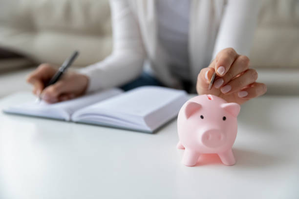 毎日の費用を書く倹約家の女性は、貯金箱にコインを入れて - high banks 写真 ストックフォトと画像