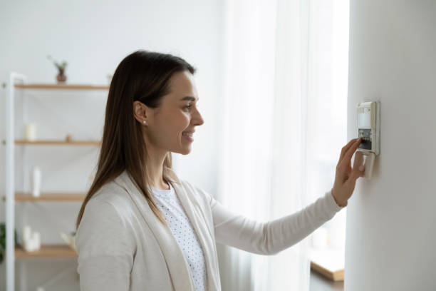 smiling woman adjusting degrees set comfortable temperature using thermostat - pushing women wall people imagens e fotografias de stock