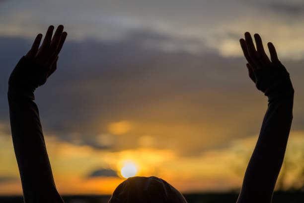 istock Person raising hands silhouetted against a sunset 1251274014