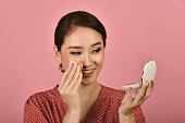 Asian woman applying makeup cosmetics while looking at the mirror, Midday face powder foundation touch up to keep looking fresh, Removing excess greasy oil.